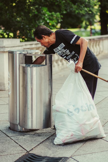 Close-up image of several black rubbish bags made of glossy plastic, tightly sealed at the top with gathered and twisted closures, positioned against a plain, light-colored wall background. The bags a